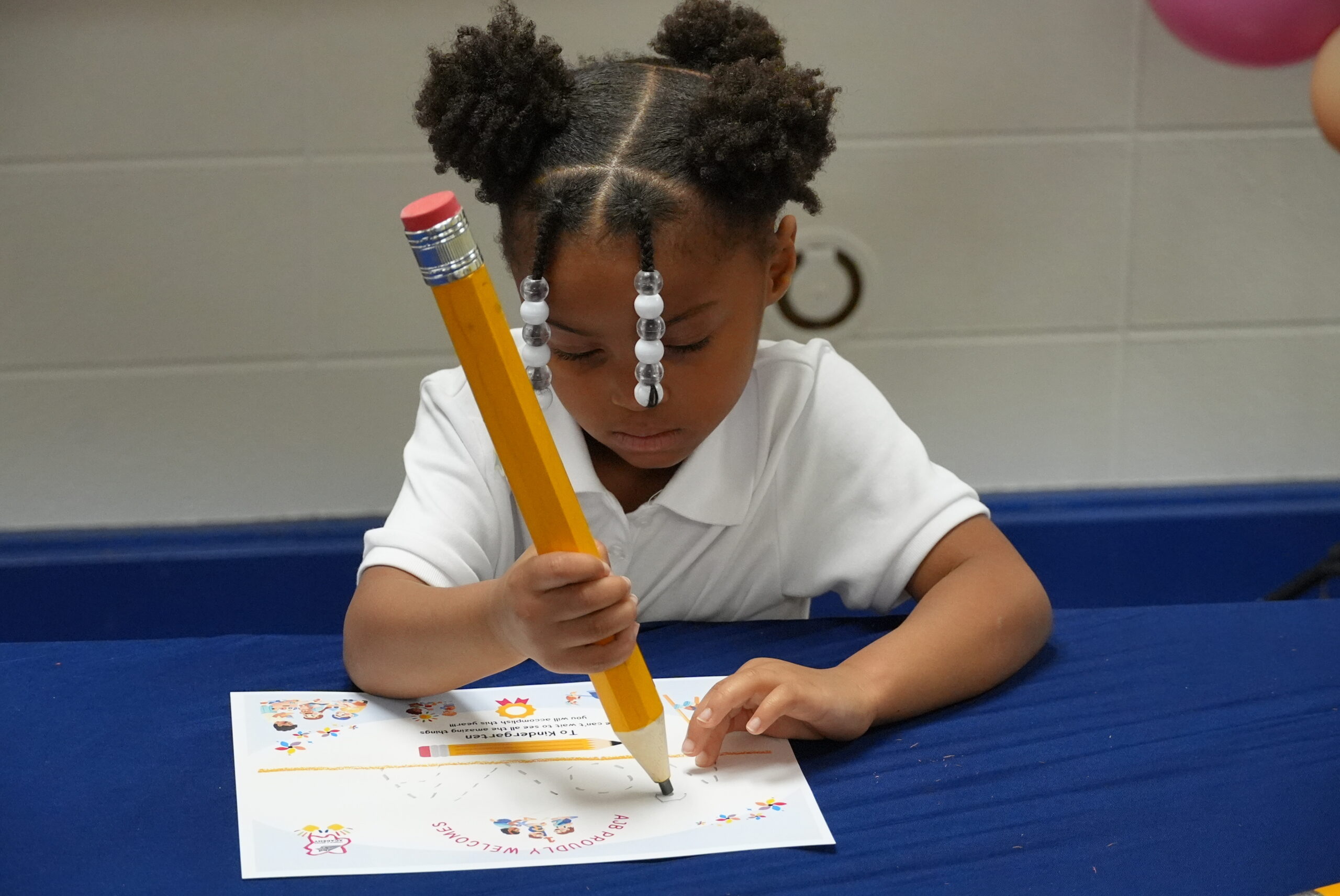 Young student practices writing with an oversized pencil during a kindergarten activity.