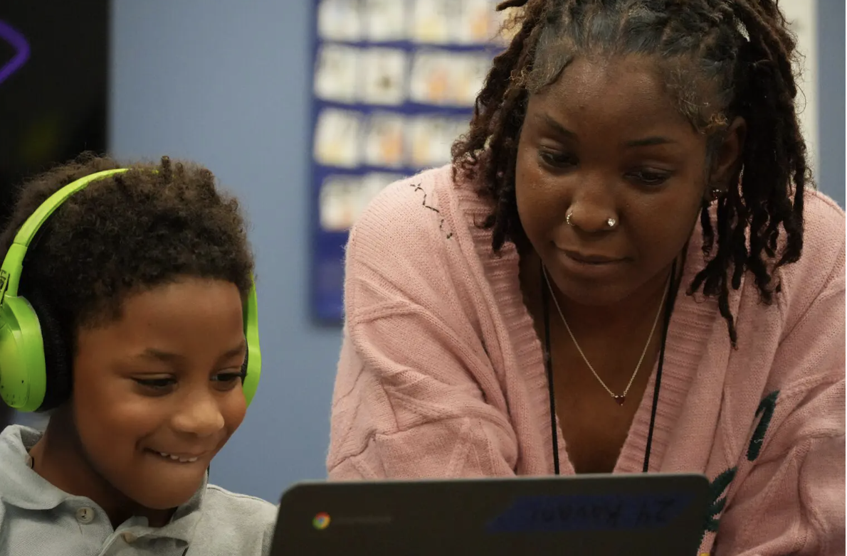 Educator assists a student wearing headphones while working on a laptop in the classroom.