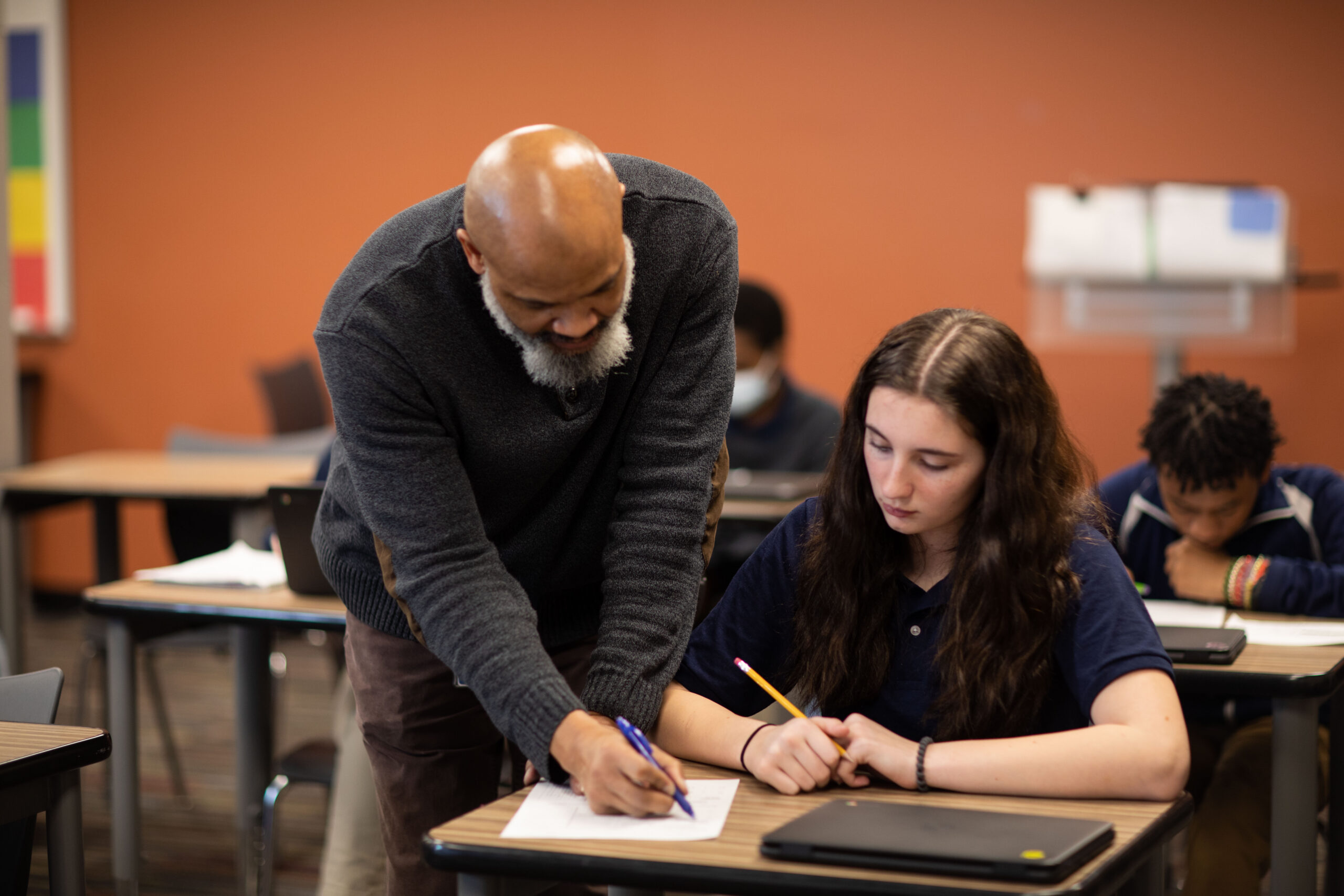 Educator provides one-on-one assistance to a student working at her desk in the classroom.