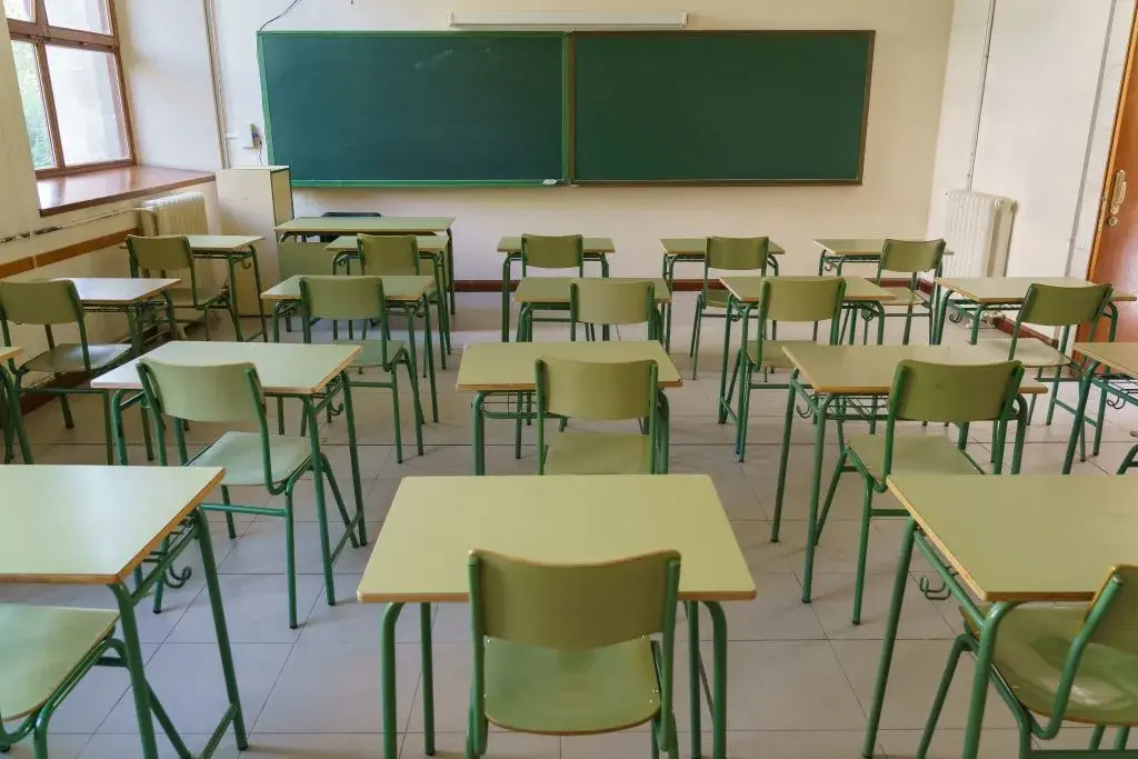 GettyImages-1220869423 Empty classroom with student desks facing a large chalkboard.