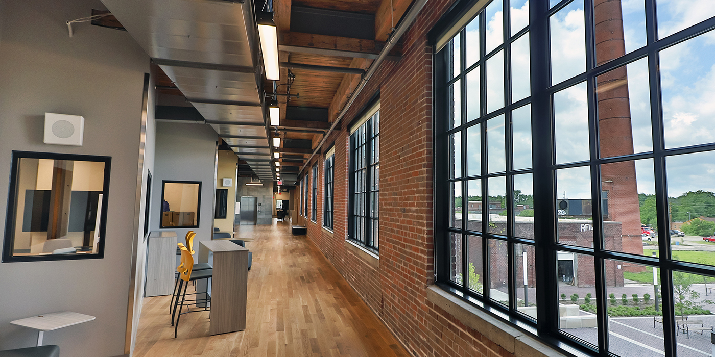 Modern school corridor with exposed brick walls, wood floors, and large windows.