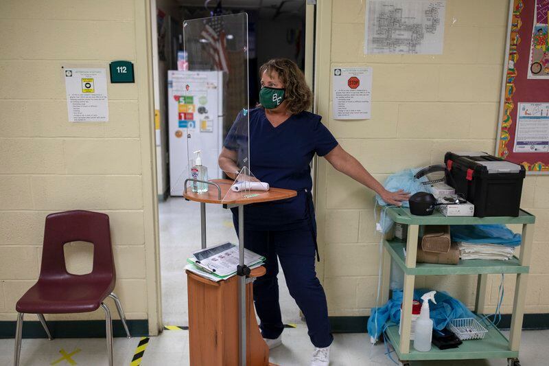School nurse wearing a face mask stands at a health station with medical supplies.