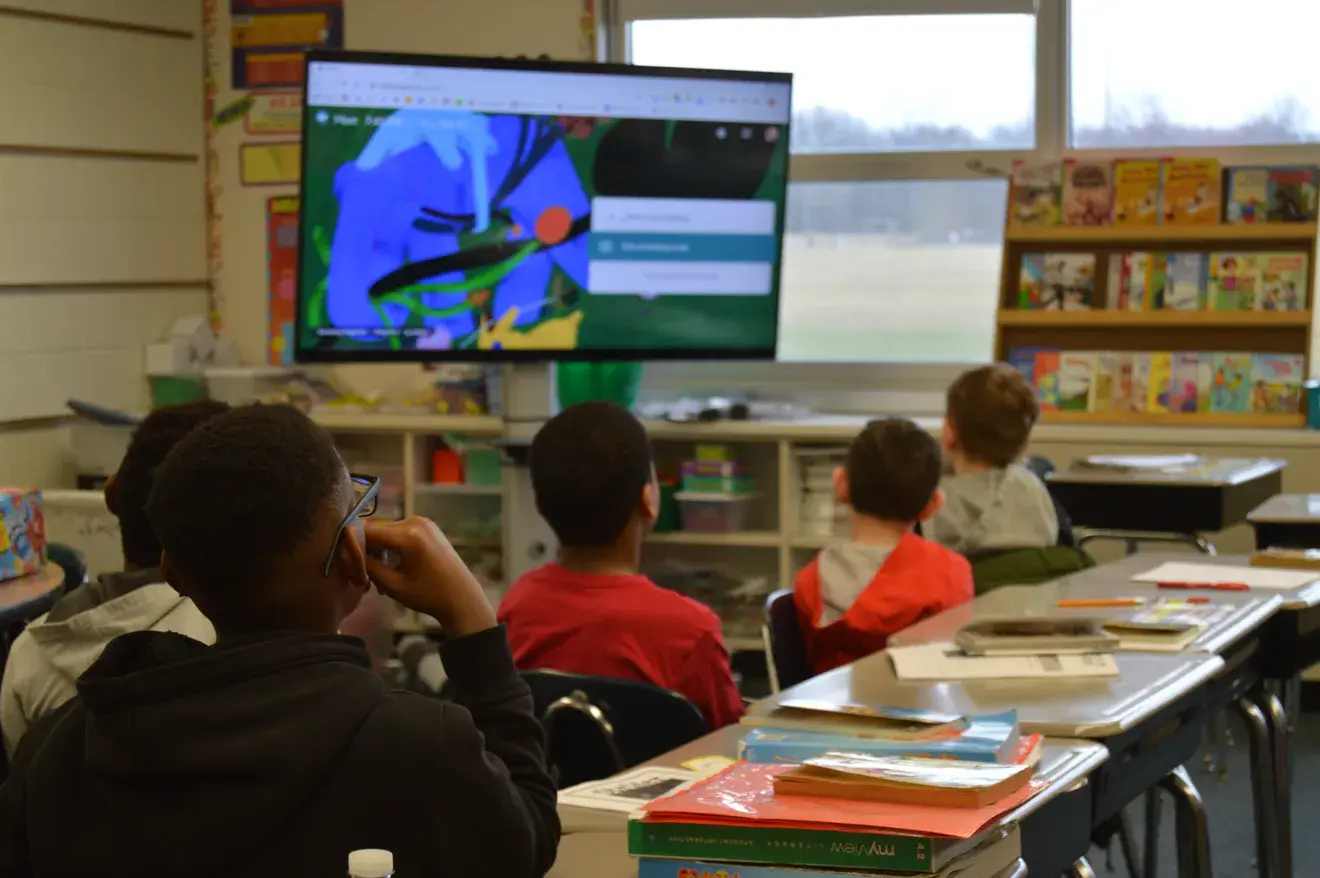 Students watch an educational presentation on a classroom screen.