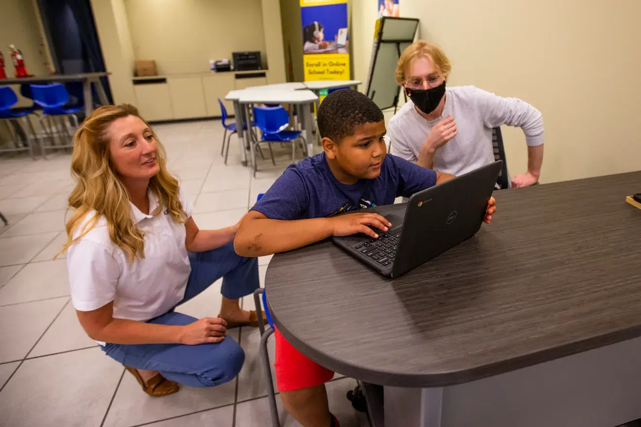 Student works on a laptop with support from two adults at My Learning Nook.