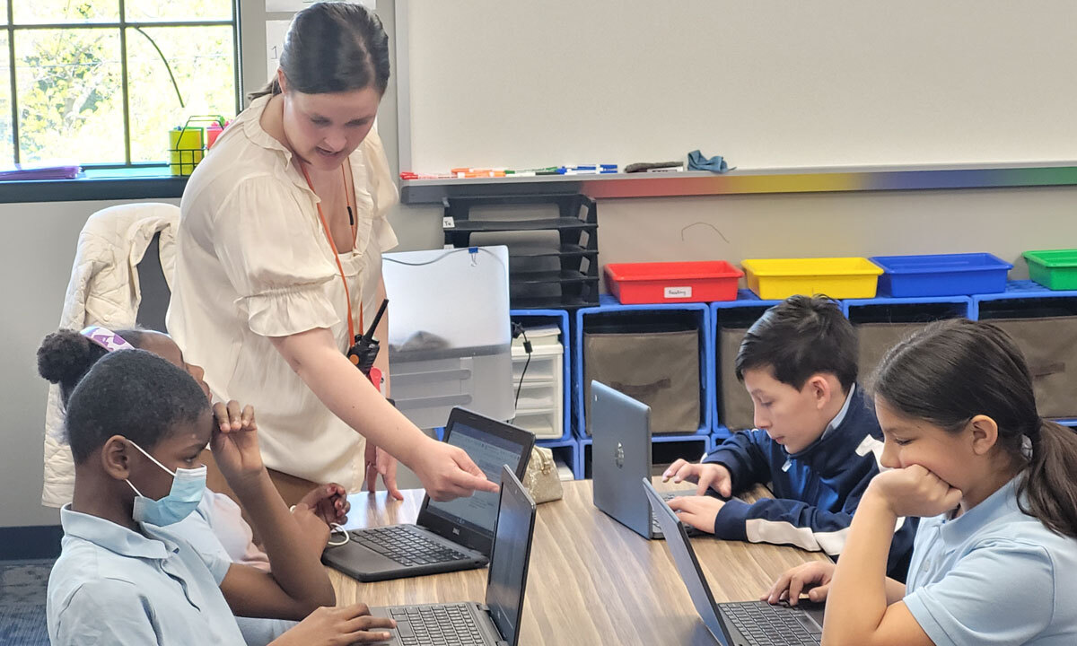 Educator assists Paramount Cottage Home students working on laptops in the classroom.