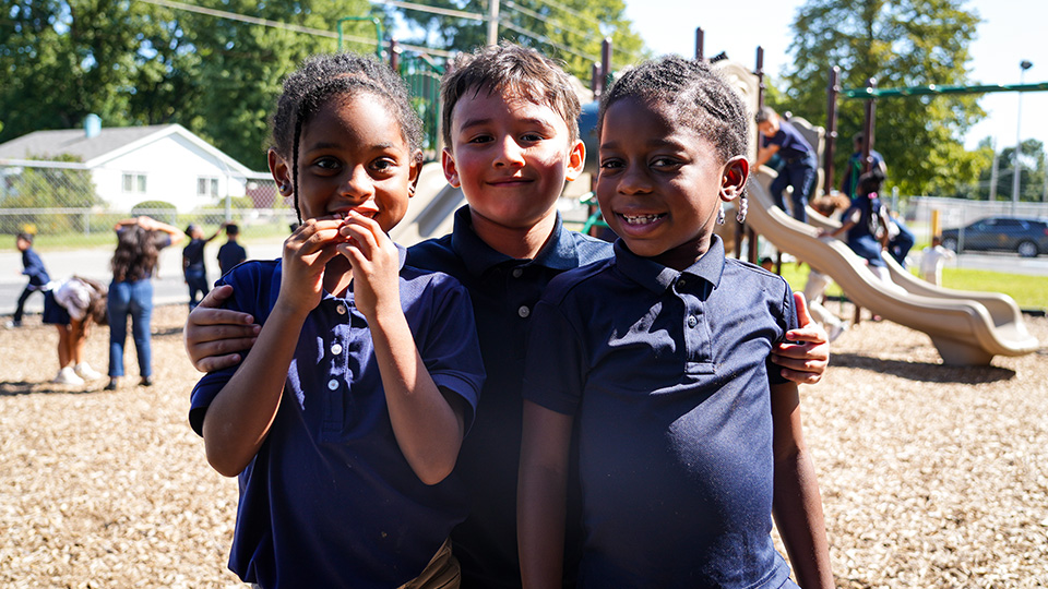 ajb-features-4 Three Andrew J. Brown Academy students smiling and posing together on the school playground during recess