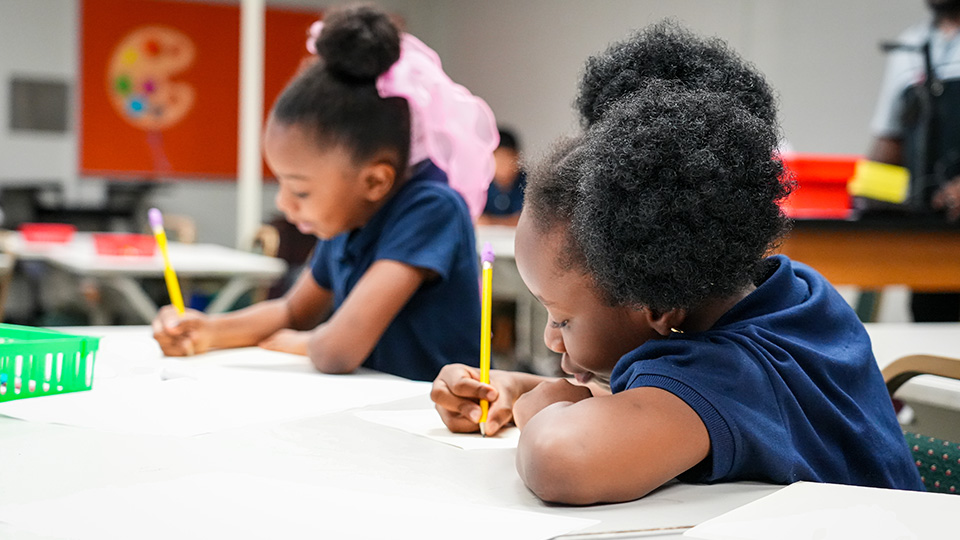 Two Andrew J. Brown Academy students concentrating on writing assignments at a classroom table