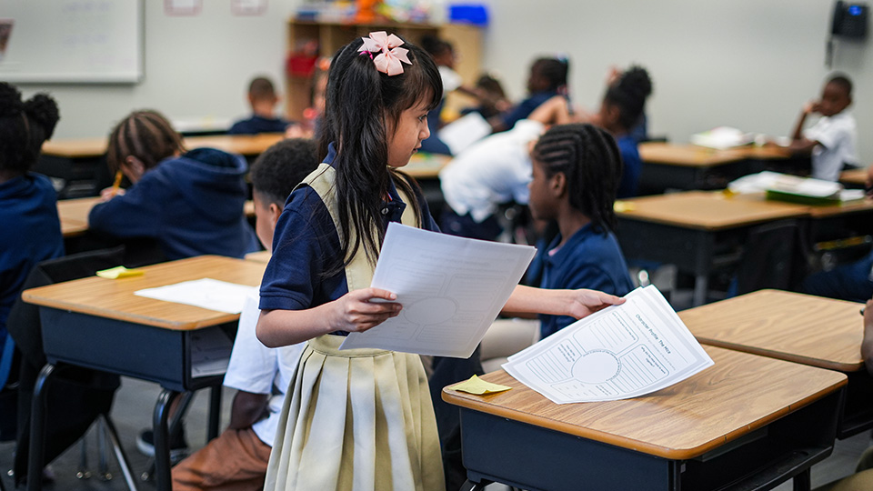 Andrew J. Brown Academy student holding worksheets while participating in a classroom learning activity with classmates