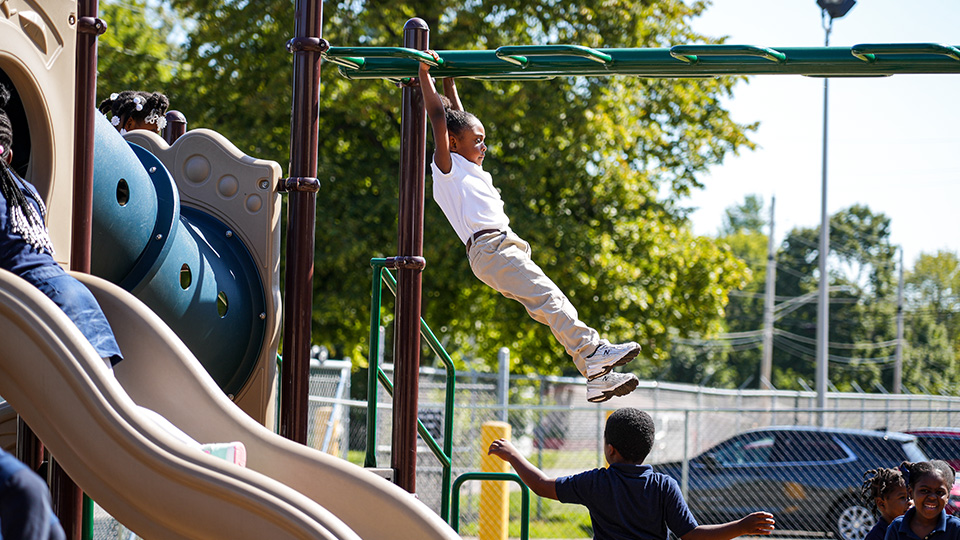 Andrew J. Brown Academy student swinging across the monkey bars while classmates play on the school playground