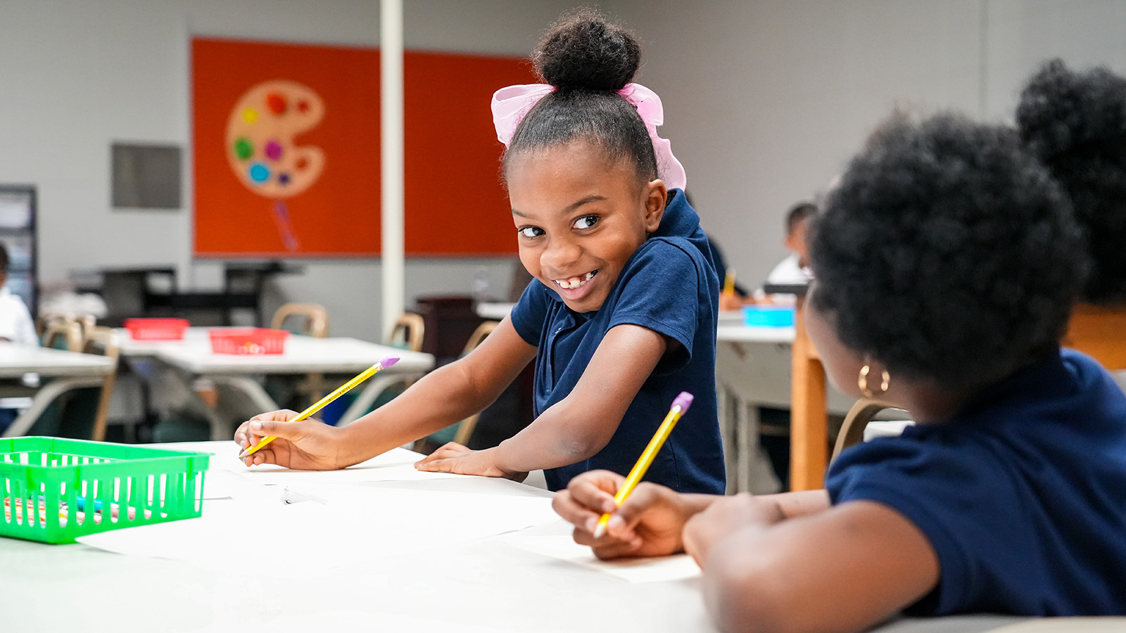 Smiling Andrew J. Brown Academy student completing a writing activity alongside a classmate at a classroom table