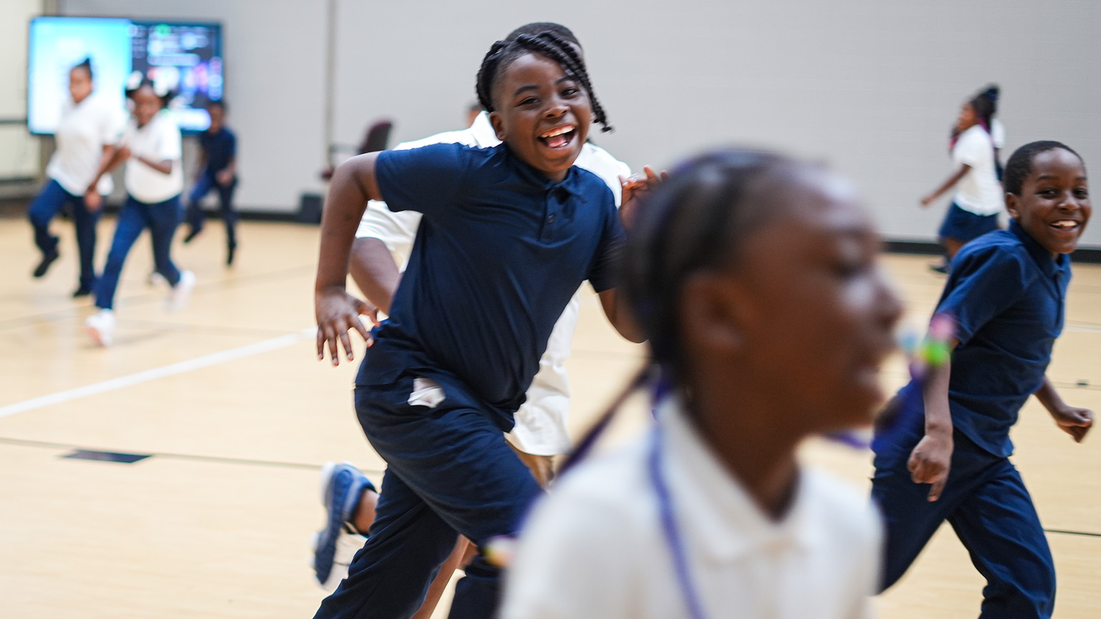 Andrew J. Brown Academy students smiling and running together during an indoor physical education activity