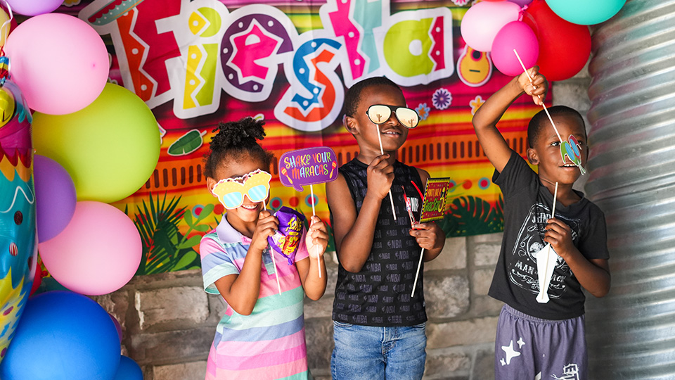 Three Paramount Brookside students posing with colorful props and balloons at a school fiesta celebration