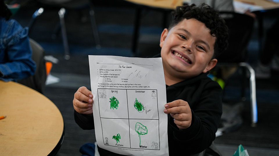 brookside-parent-center-2 Smiling Paramount Brookside student holding up a completed four seasons worksheet in the classroom