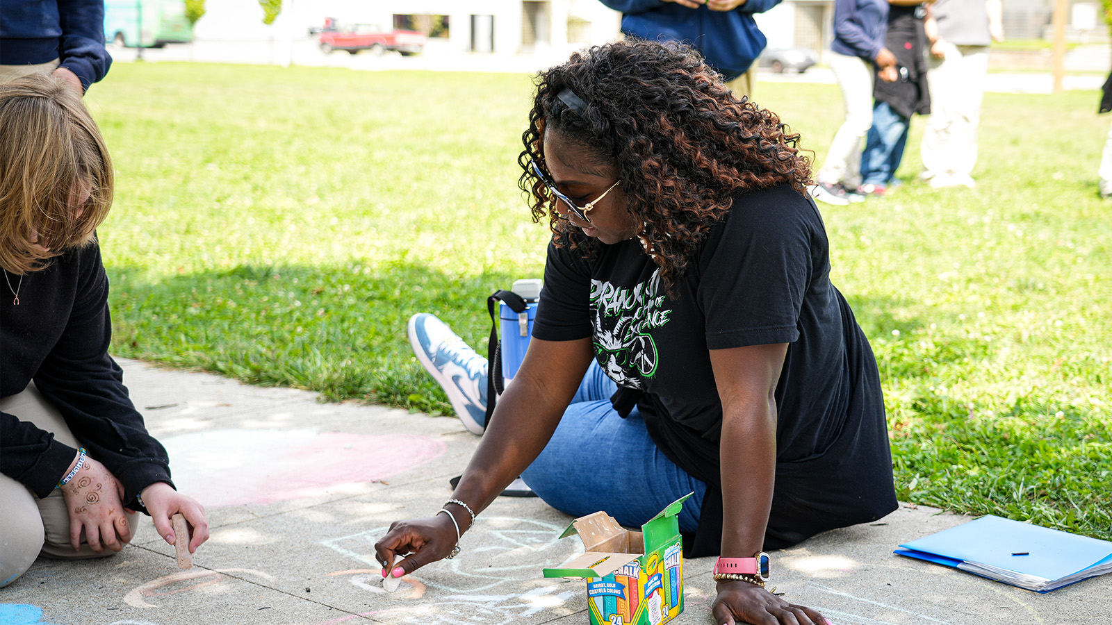 Paramount staff member creating sidewalk chalk art with students during an outdoor school activity