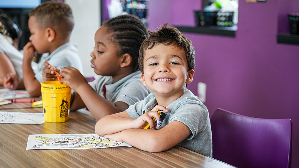 Smiling Paramount Cottage Home student sitting at a classroom table with classmates during a coloring activity