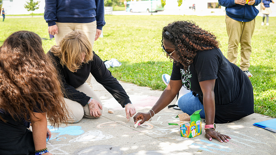Paramount Englewood students and staff creating colorful sidewalk chalk drawings together during an outdoor school activity