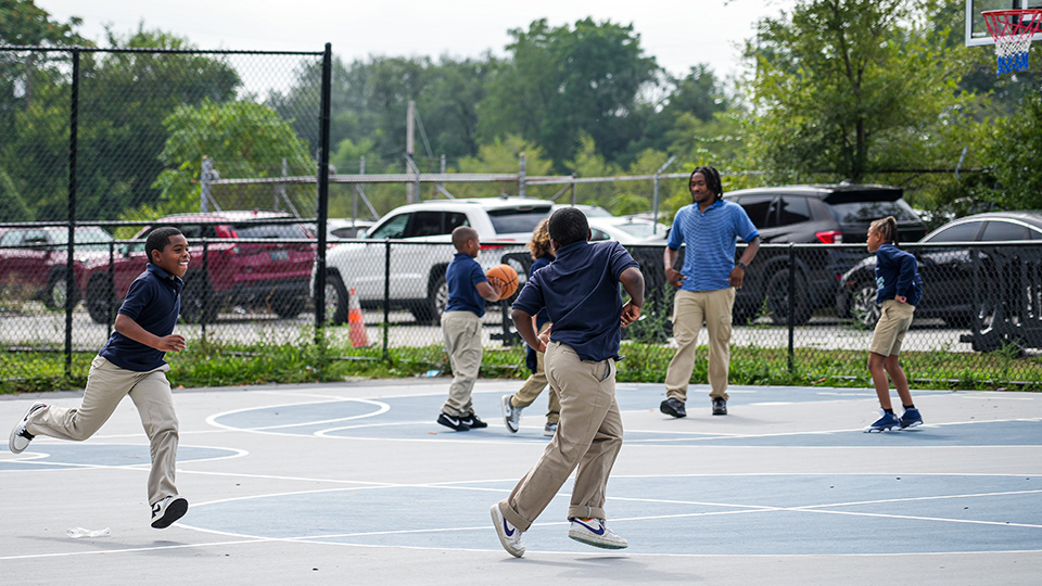 Paramount Englewood students playing basketball on the outdoor school court with a staff member supervising
