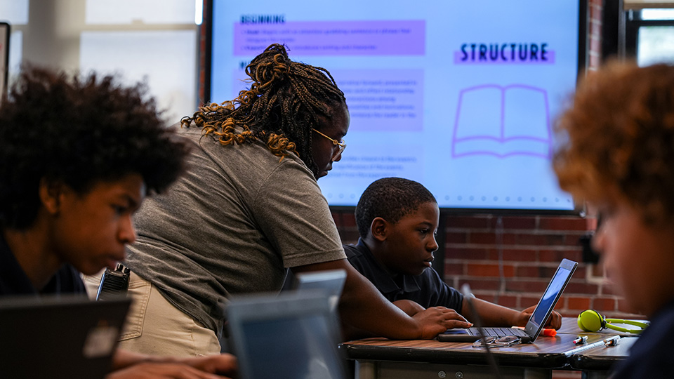 Paramount Englewood teacher helping a student with a laptop during a classroom lesson