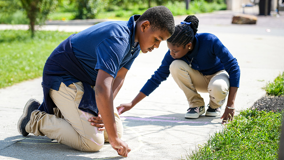 Two Paramount students creating sidewalk chalk drawings together outside their school
