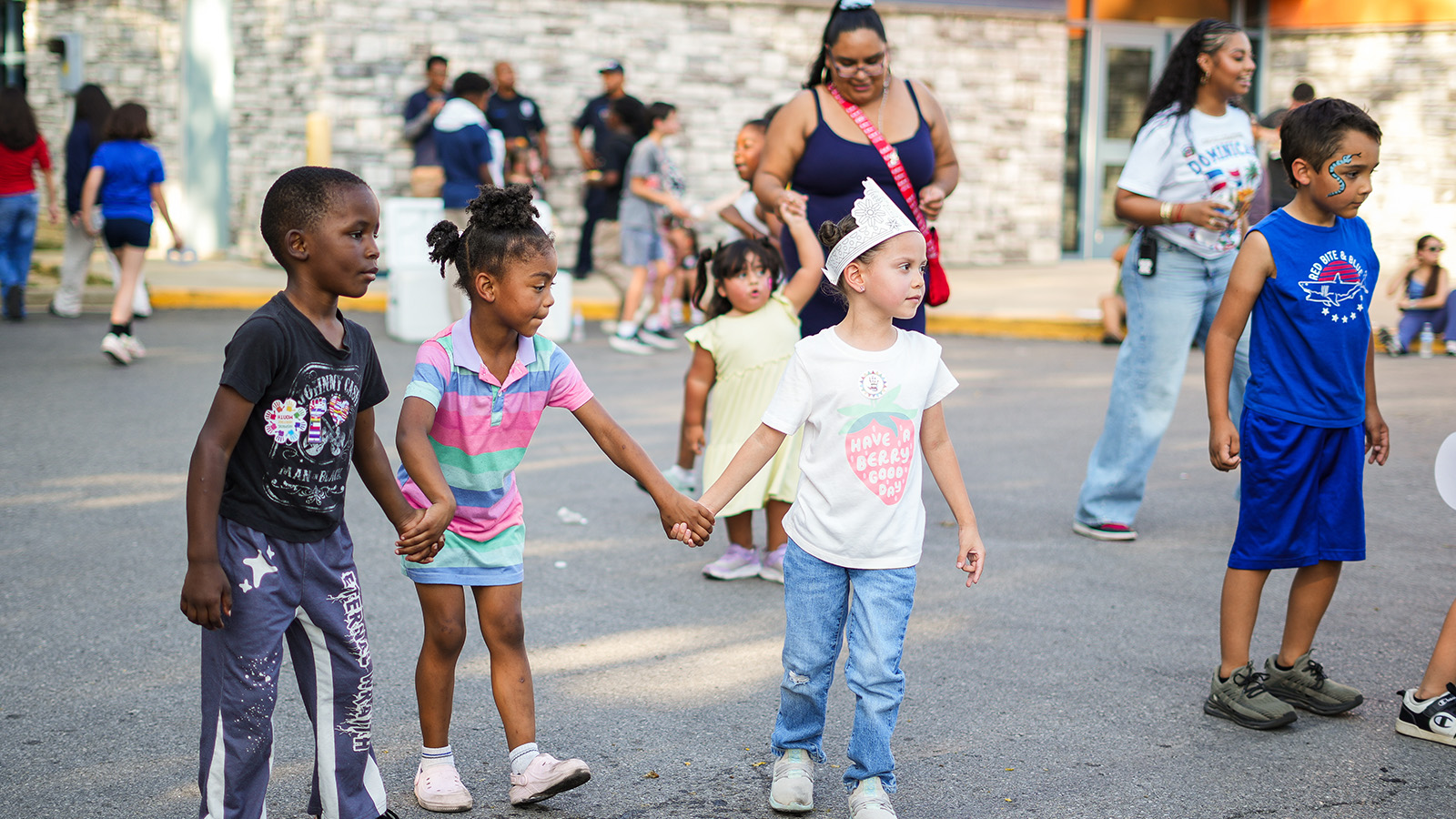 Children holding hands and enjoying an outdoor school event with families and community members