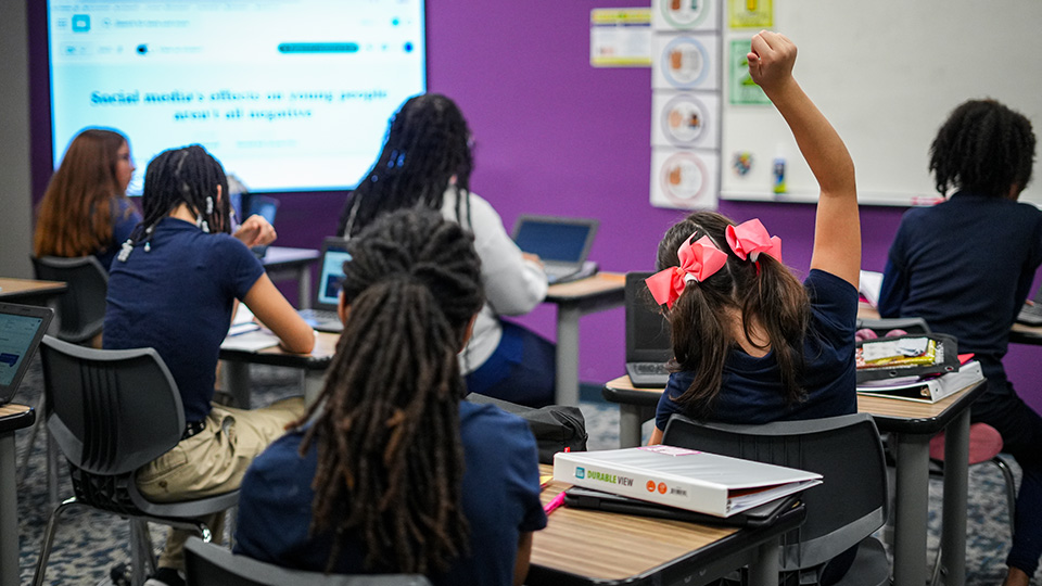 Girls IN STEM Academy students participating in a classroom lesson with laptops as a student raises her hand
