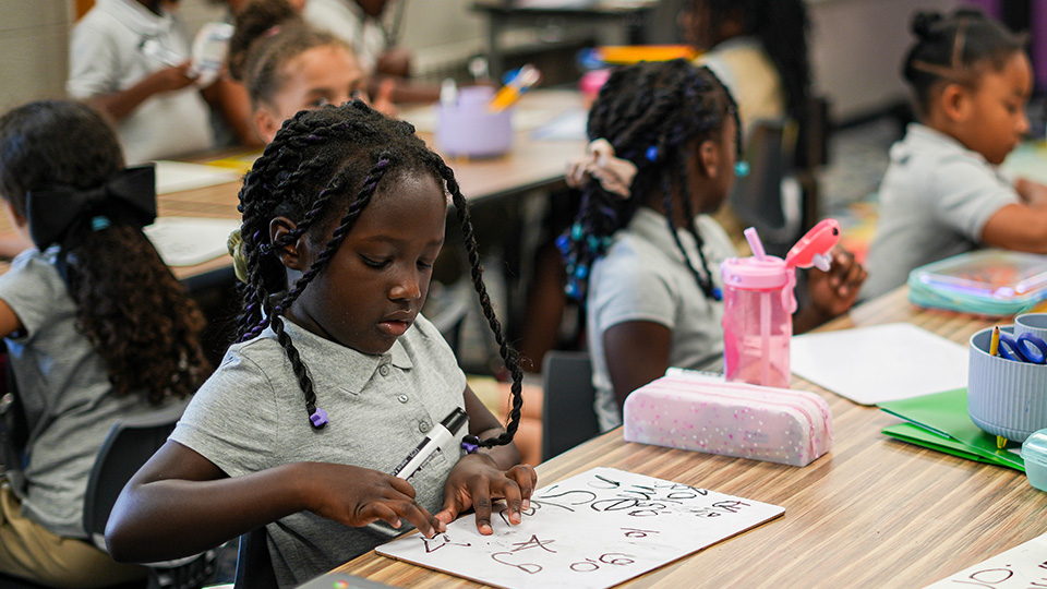 Girls IN STEM Academy student practicing writing on a whiteboard during a classroom learning activity