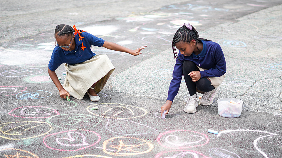 Two Girls IN STEM Academy students creating colorful sidewalk chalk drawings together outdoors