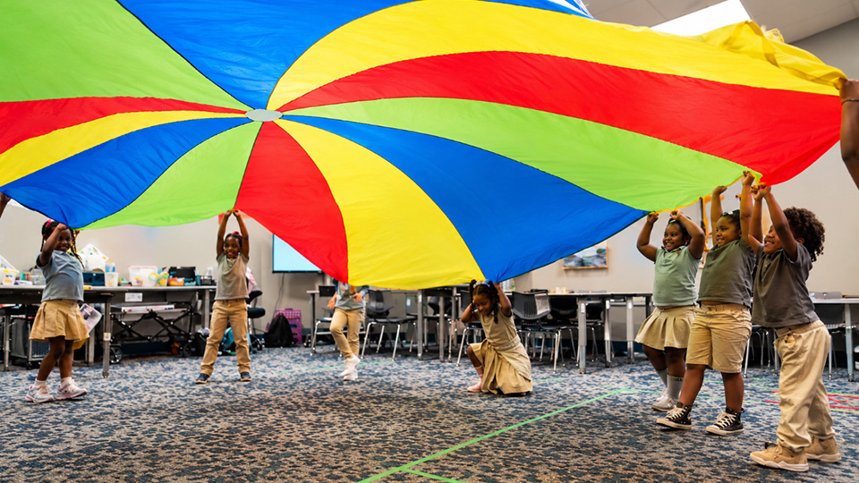 Girls IN STEM Academy students participating in a colorful parachute activity together indoors
