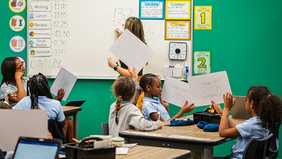 Girls IN STEM Academy students holding up their completed worksheets during an interactive classroom lesson