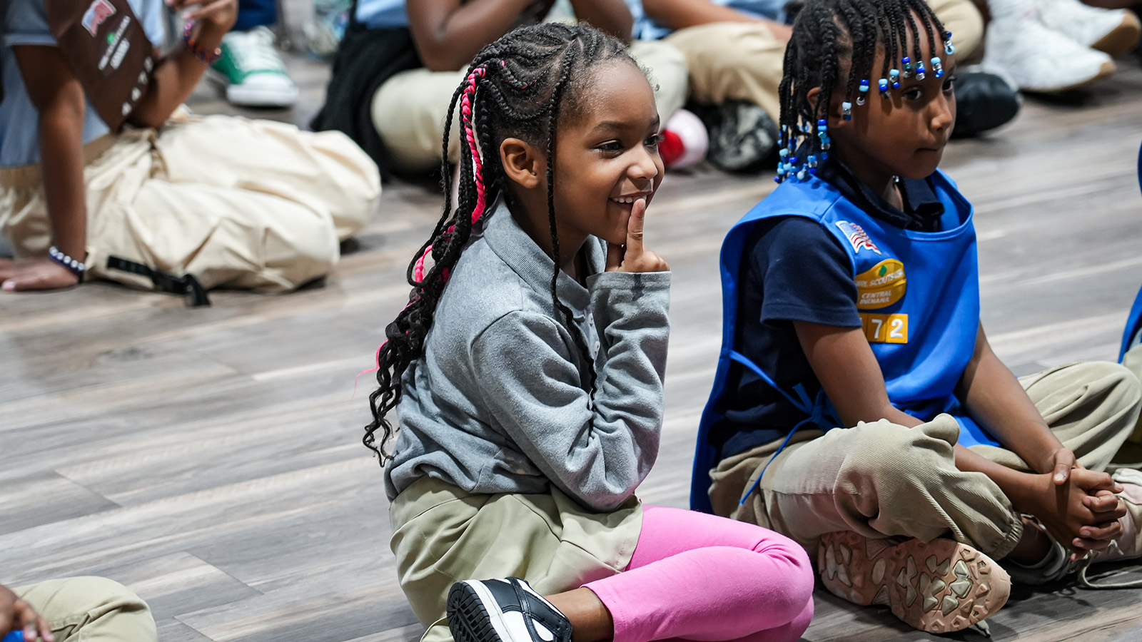 gisa-contact-hero-updated Girls IN STEM Academy students sitting together and listening during a group activity, with one student smiling and another wearing a blue scouting vest