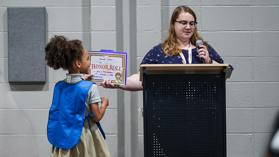 Girls IN STEM Academy student receiving an Honor Roll certificate from a teacher during a school awards ceremony
