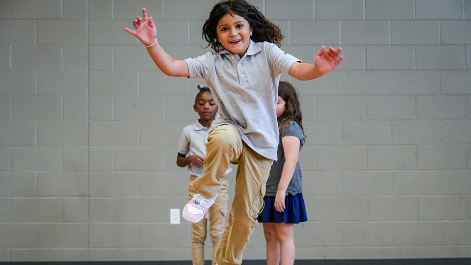 Paramount Lafayette student jumping and smiling during a physical education activity in the school gymnasium