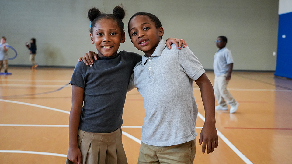 Two Paramount Lafayette students smiling and posing together with their arms around each other in the school gymnasium