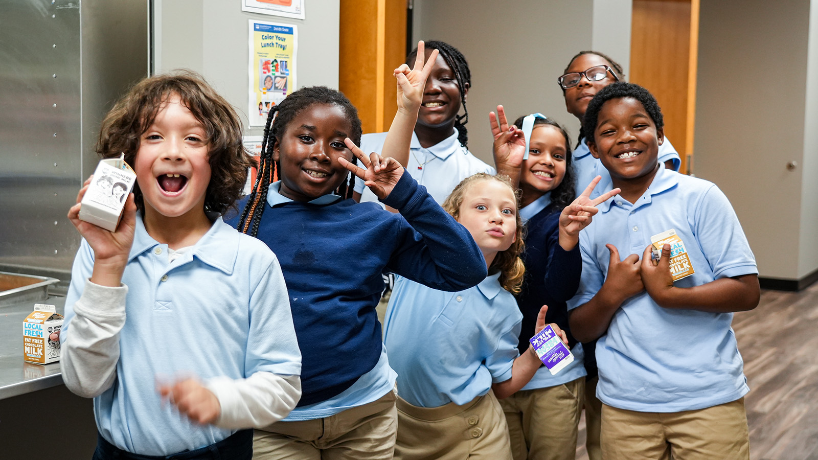 Smiling Paramount Lafayette students posing together and flashing peace signs while holding milk cartons in the school cafeteria