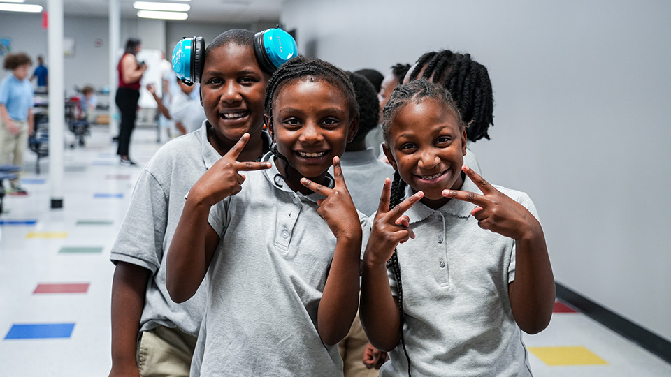 Three smiling Paramount Lafayette students posing together and flashing peace signs in the school hallway