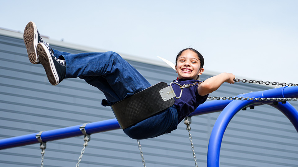 Paramount Lafayette student smiling while swinging high on the school playground during outdoor recess