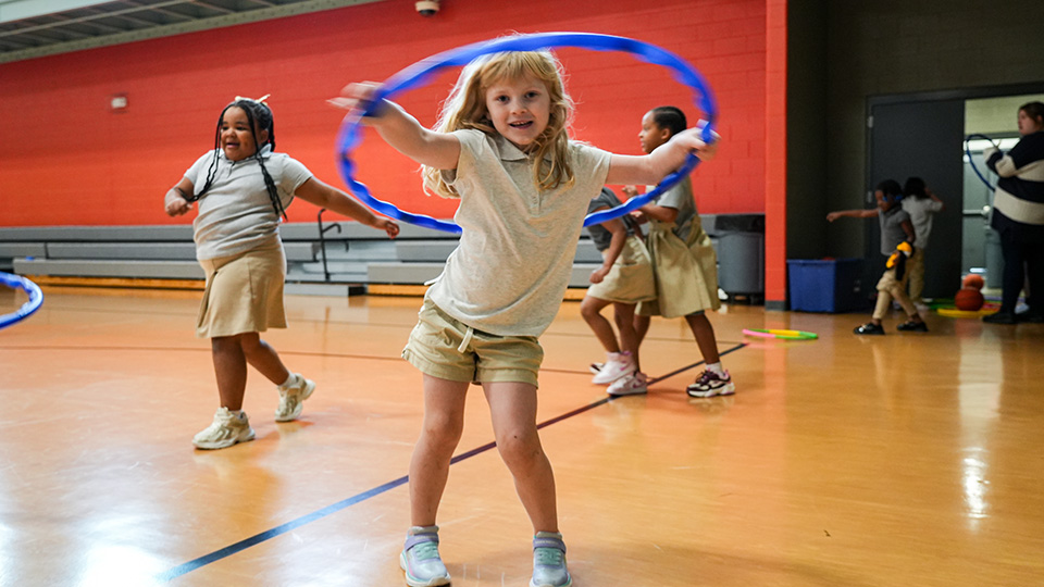 Paramount Lafayette students playing with hula hoops during a physical education activity in the school gymnasium