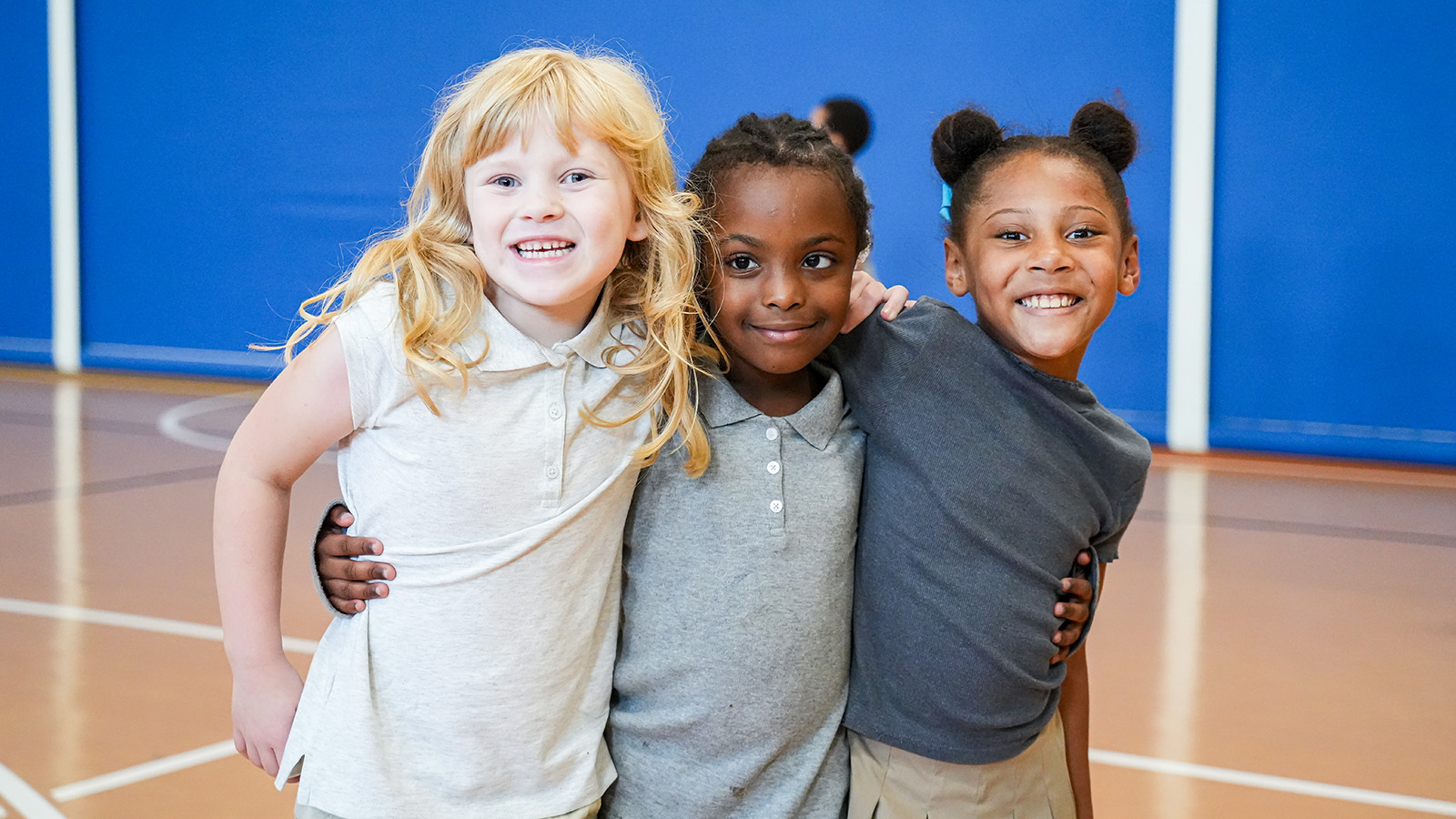 Three smiling Paramount Lafayette students posing together with their arms around each other in the school gymnasium