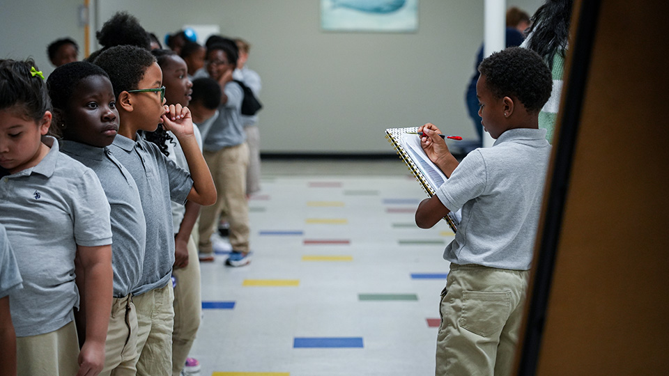 Paramount Lafayette student writing on a clipboard while classmates line up in the school hallway