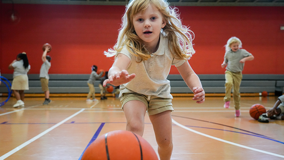 Paramount Lafayette student reaching for a basketball during a physical education activity in the school gymnasium while classmates play in the background
