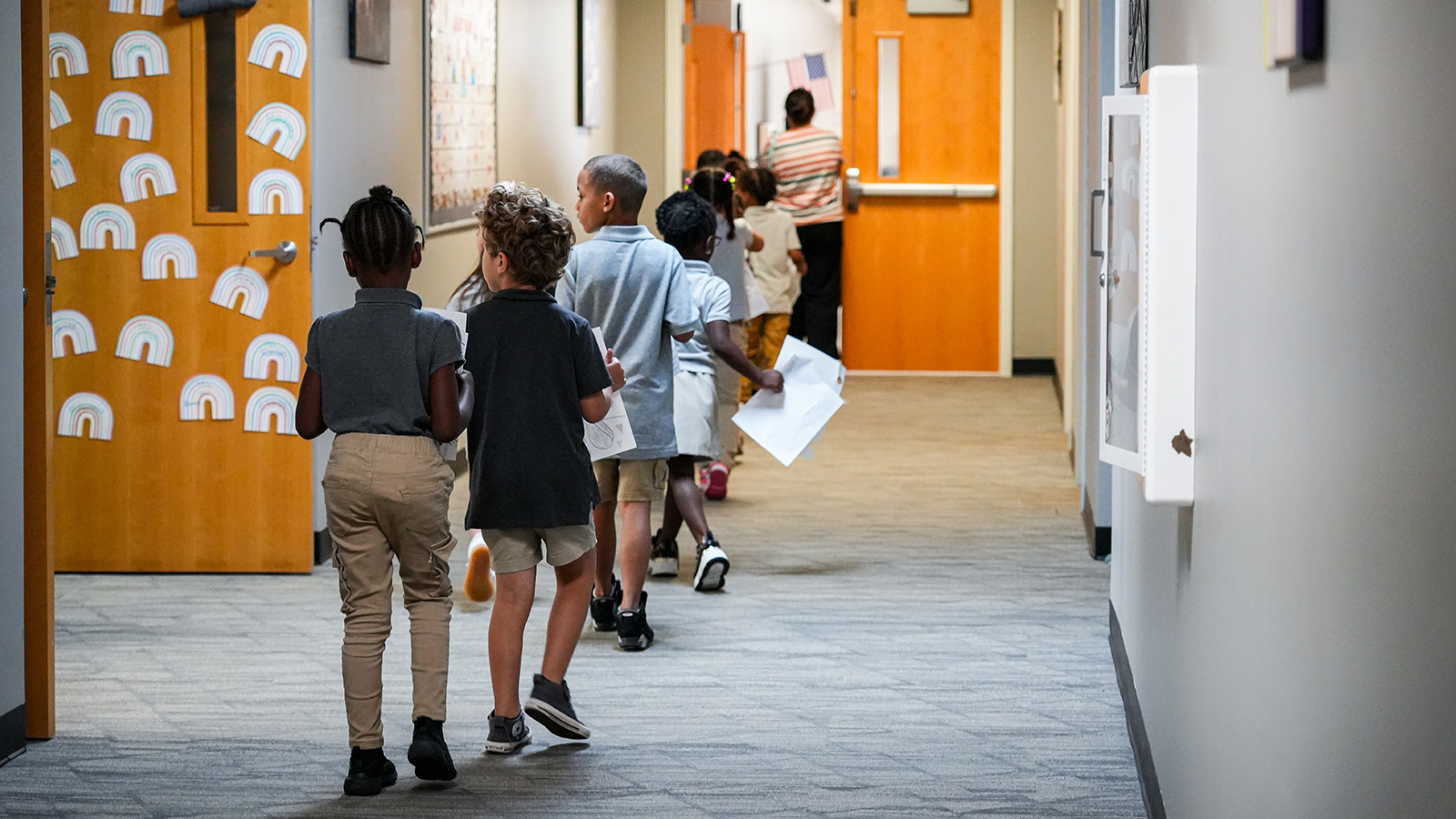 Paramount Lafayette students walking through the school hallway carrying worksheets as a staff member leads the way