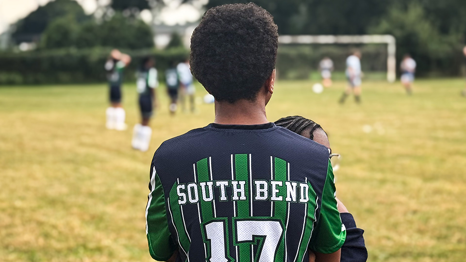 Paramount South Bend soccer player wearing a team jersey while watching teammates play on the field