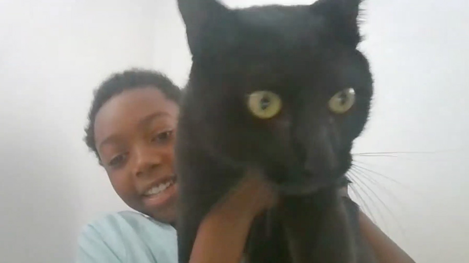 Paramount Online Academy student smiling while holding a black cat up to the camera during a virtual learning activity