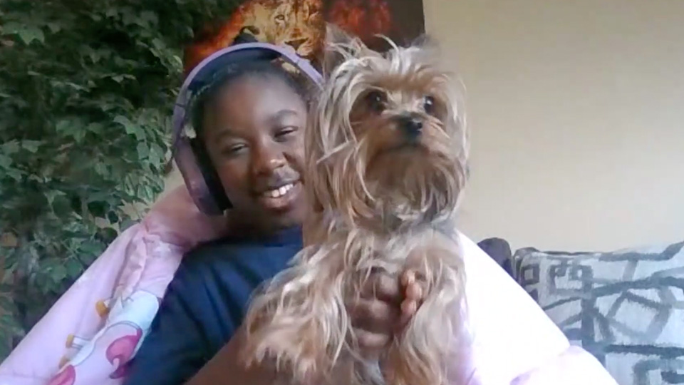 Paramount Online Academy student smiling while holding her small dog during a virtual learning session from home