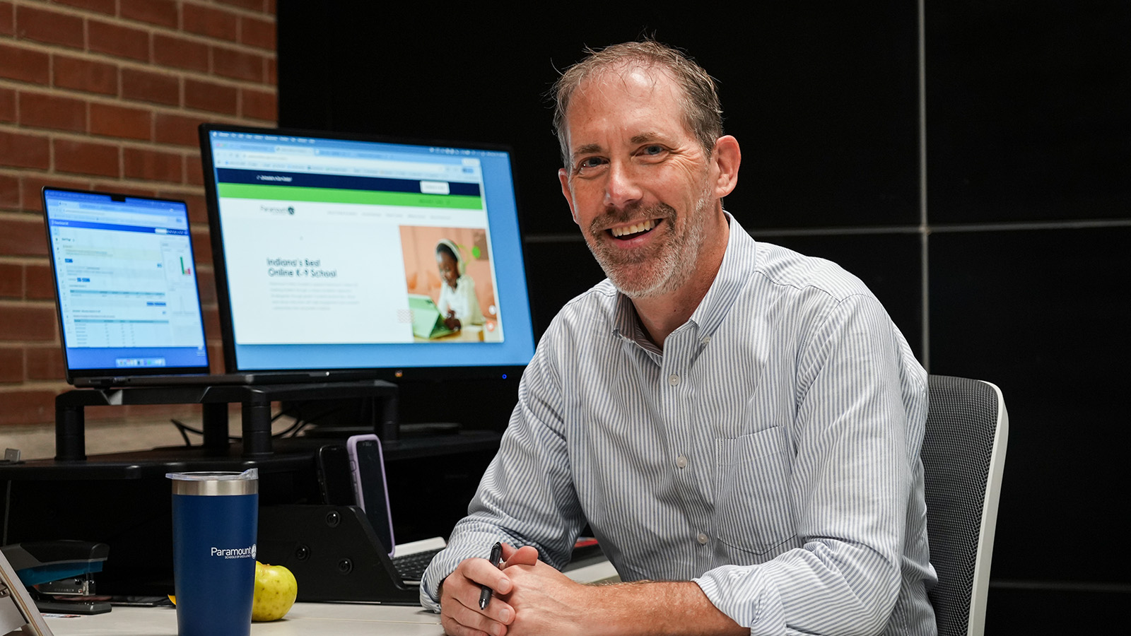 online-academy-staff-hero Smiling Paramount Online Academy principal, Anthony Brose, seated at his desk with computer monitors in the background