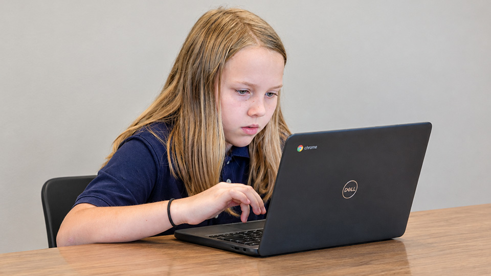 Paramount Online Academy student concentrating on her schoolwork using a Chromebook laptop.
