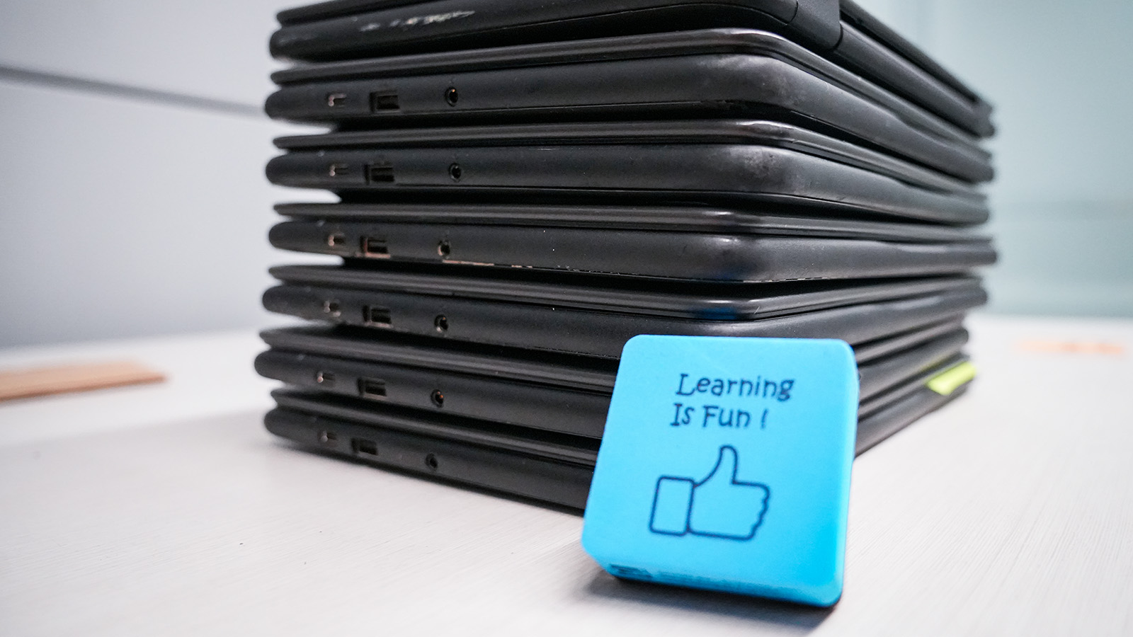 Stack of laptops for Paramount Online Academy students beside a blue "Learning Is Fun!" sign
