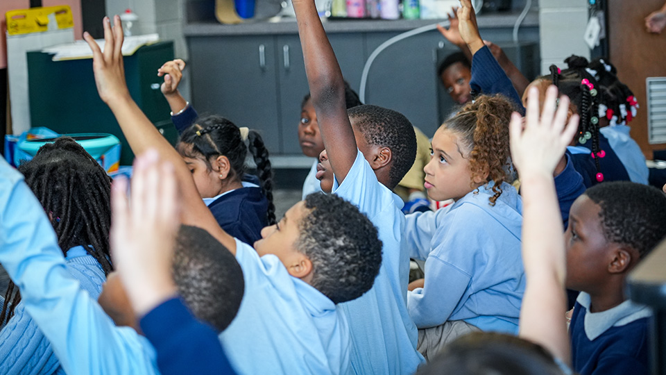 Paramount South Bend students enthusiastically raising their hands to participate in an interactive classroom lesson