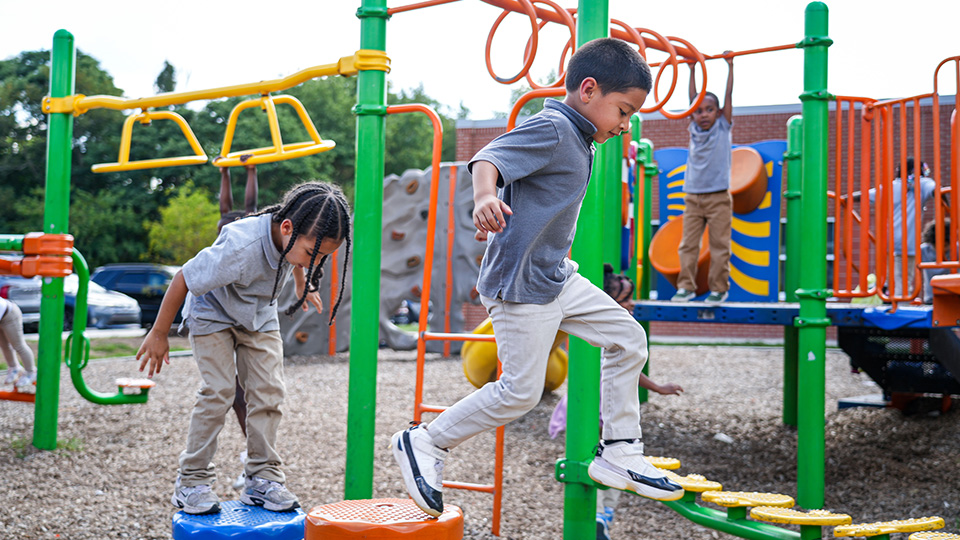 Paramount South Bend students climbing, balancing, and playing on colorful playground equipment during outdoor recess