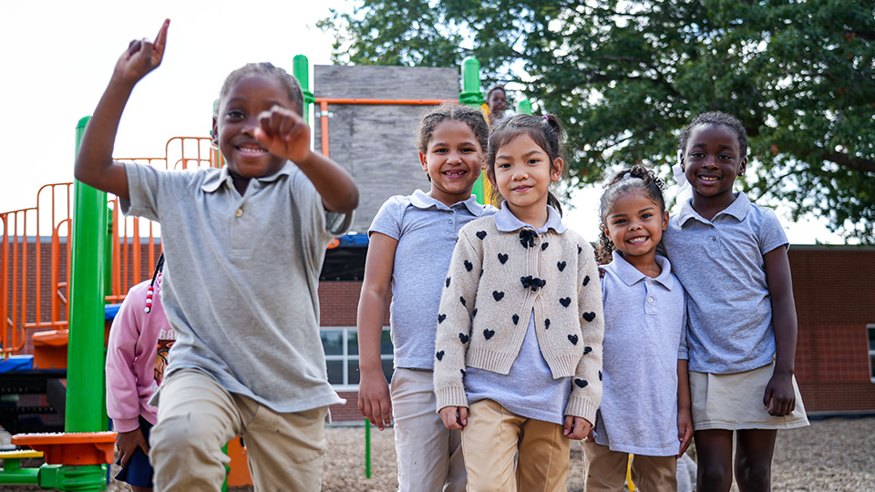 Paramount South Bend students smiling and posing together in front of colorful playground equipment during outdoor recess
